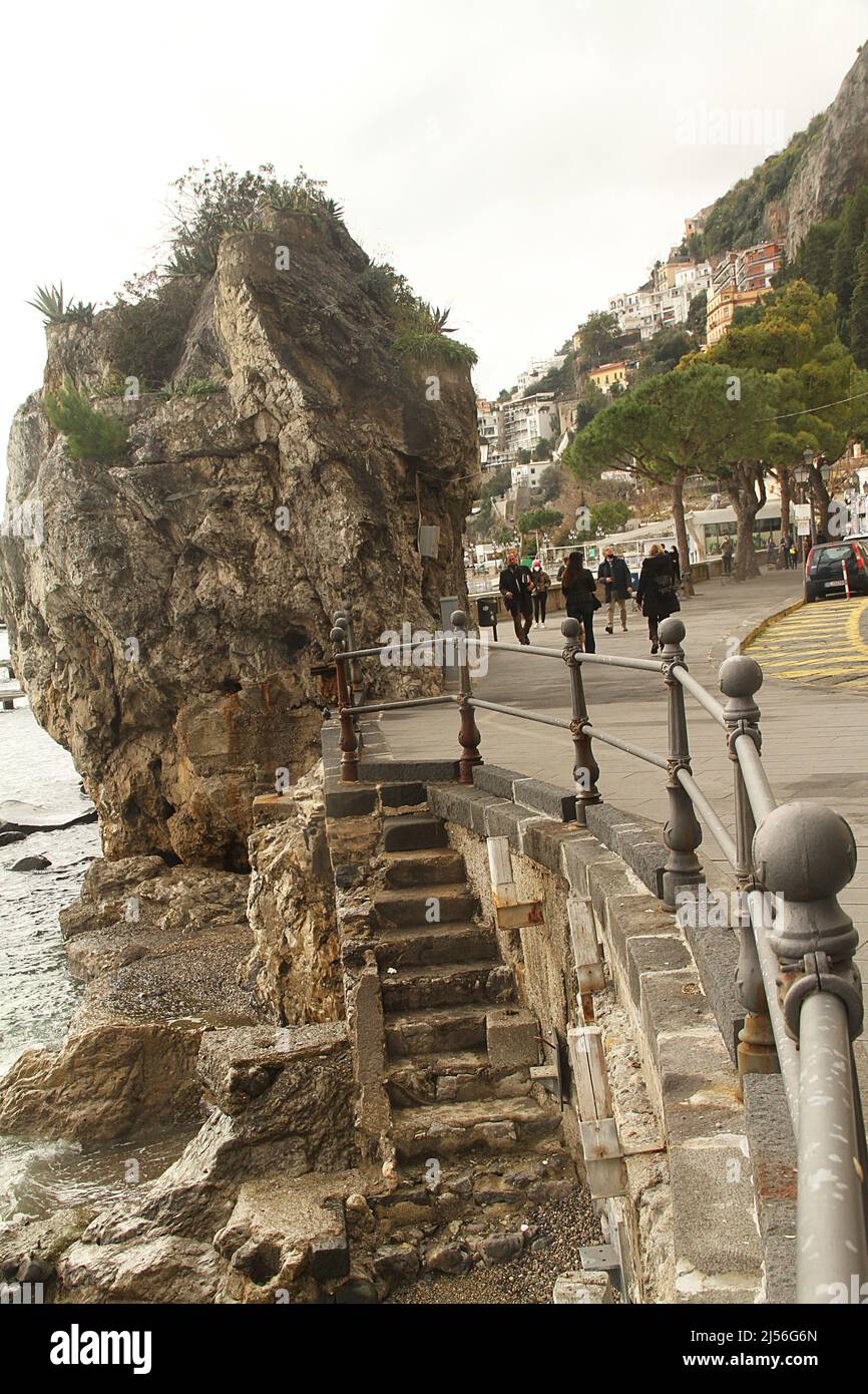 Amalfiküste, Italien. Menschen, die entlang der Via Lungomore dei Cavalieri spazieren. Große Felsbrocken am Ufer und Steinstufen, die zum Wasser führen. Stockfoto