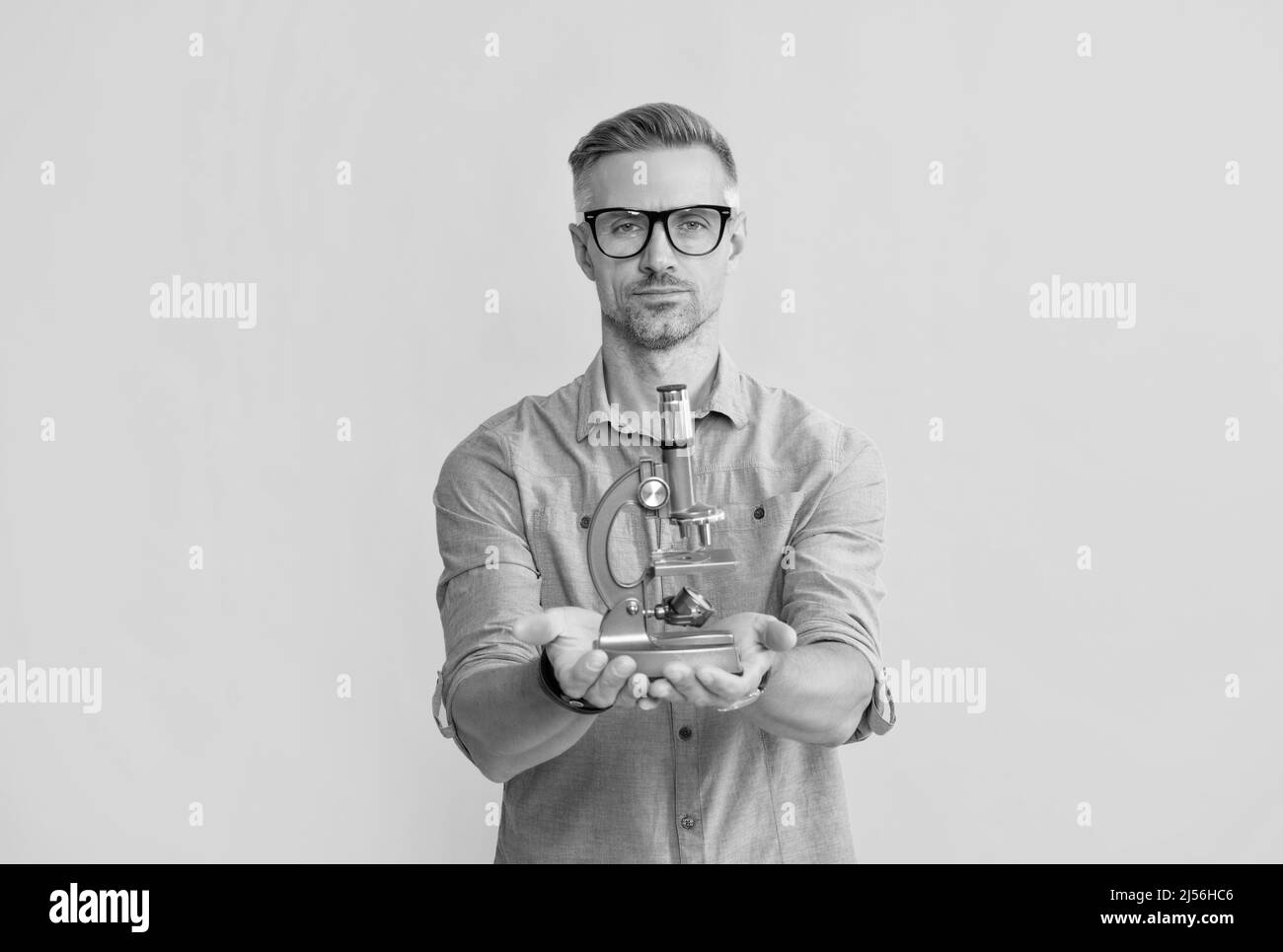 Mann in einer Brille hält Mikroskop auf gelbem Hintergrund, Data Science Stockfoto