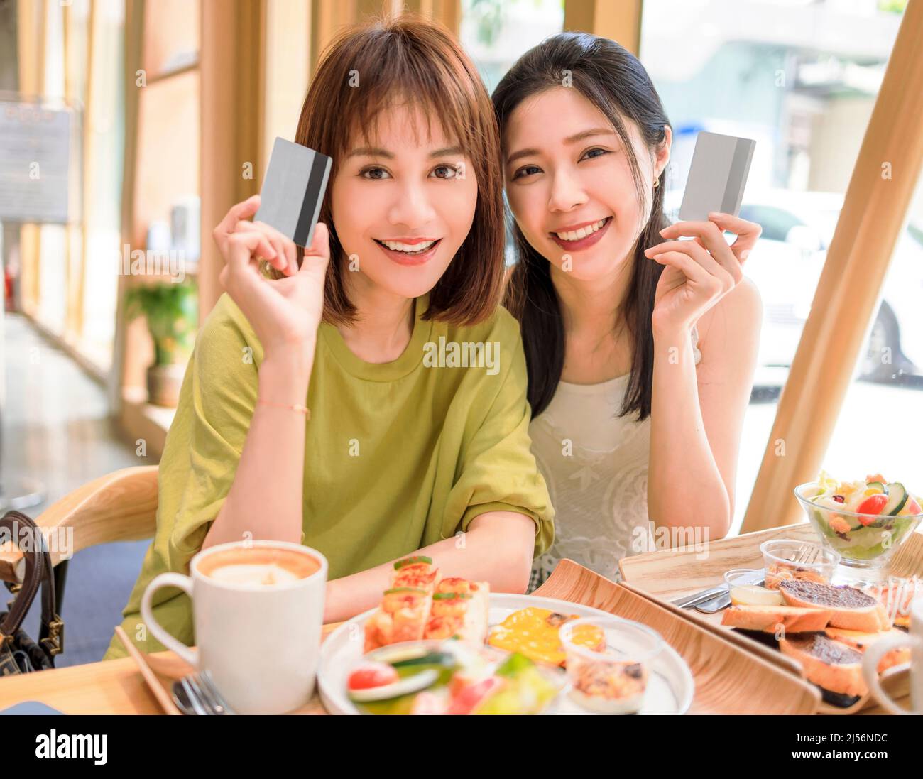 Glückliche, schöne junge Frauen, die die Kreditkarte im Restaurant vorführen Stockfoto