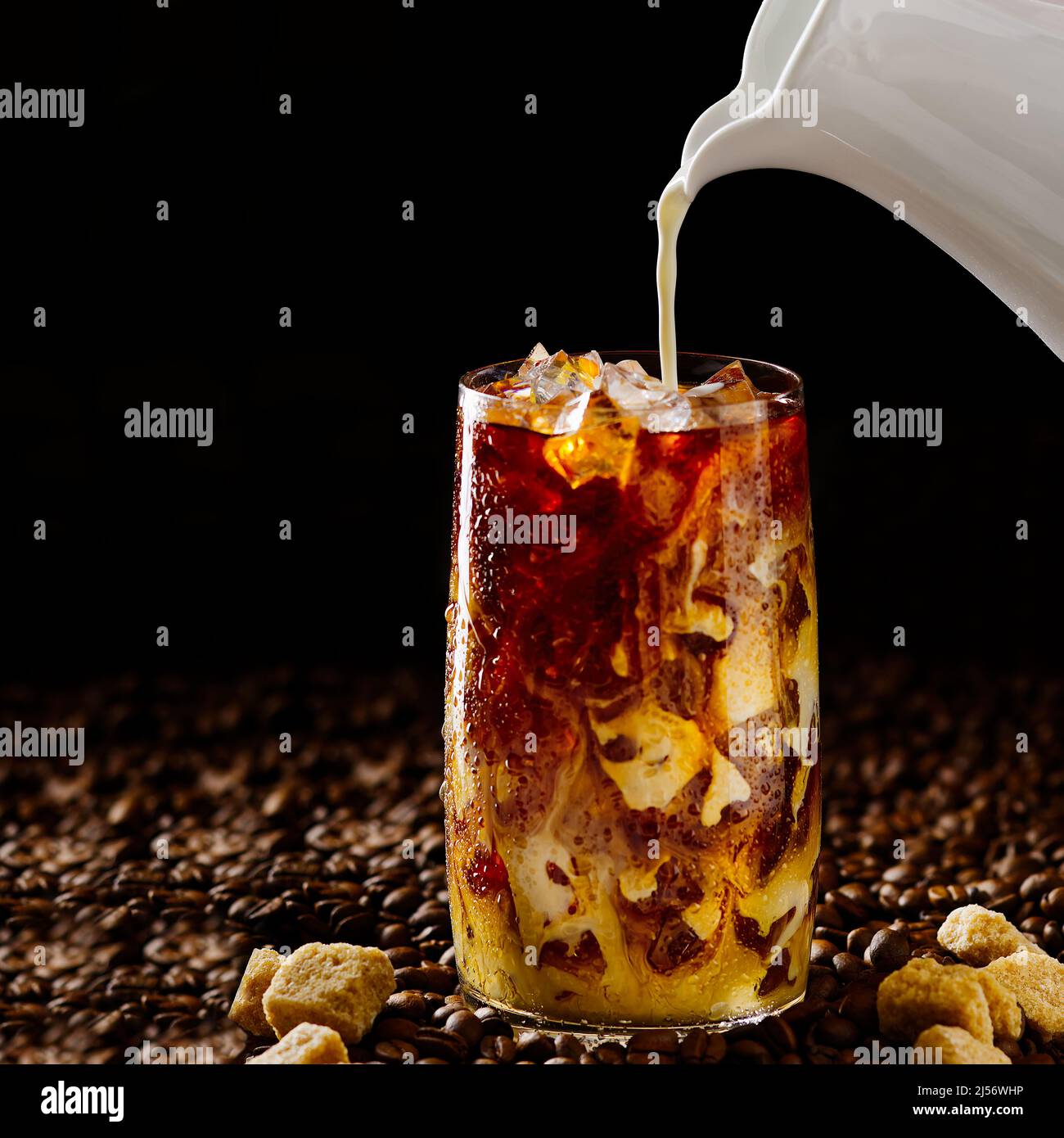 Eiskaffee. Leckerer Eiskaffee mit Milch, kaltes Getränk im Glas mit Eis auf dunklem Kaffeehintergrund. Stockfoto