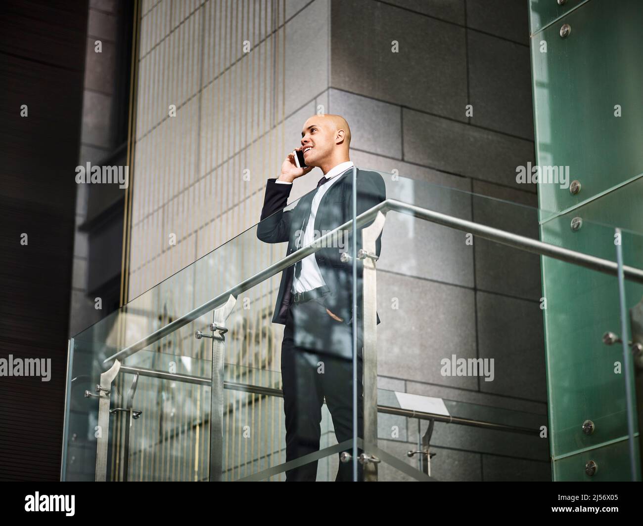 Ein junger latino-Geschäftsmann, der auf einer Treppe steht und mit dem Mobiltelefon in einem modernen Bürogebäude telefoniert Stockfoto