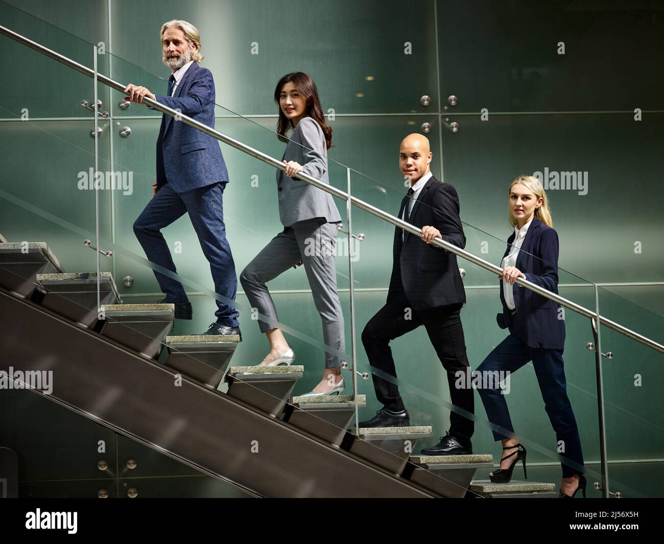 Multinationale und multiethnische Geschäftsleute Männer und Frauen, die in einer Schlange in einem modernen Bürogebäude die Treppe hochgehen und die Kamera betrachten. Stockfoto