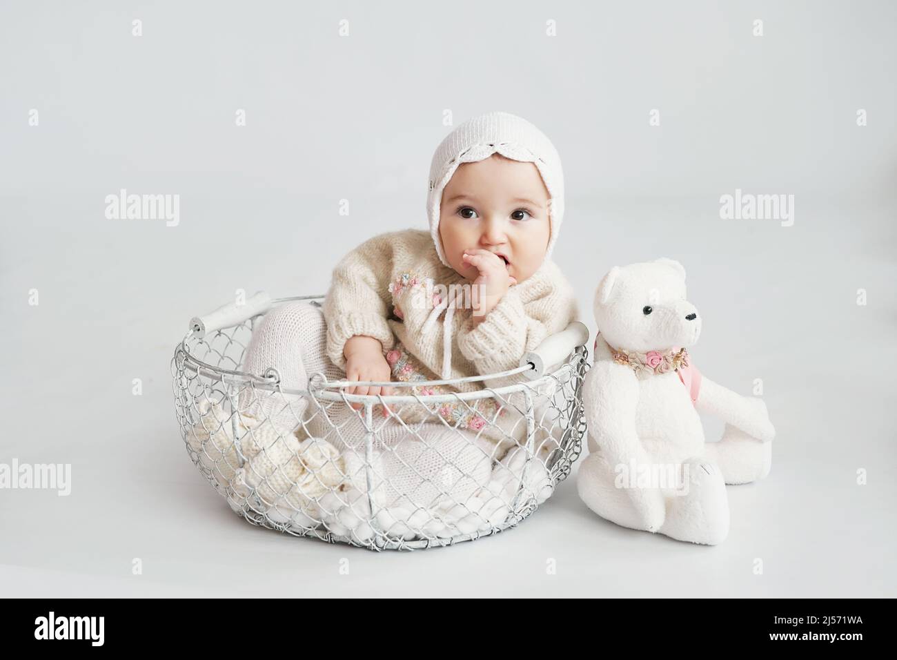 Nettes Baby Mädchen in Strickkleidung und Hut mit Teddybär Spielzeug. Kinderschutztag. Grußkarte zum Muttertag. Internationaler Tag des Glücks Stockfoto