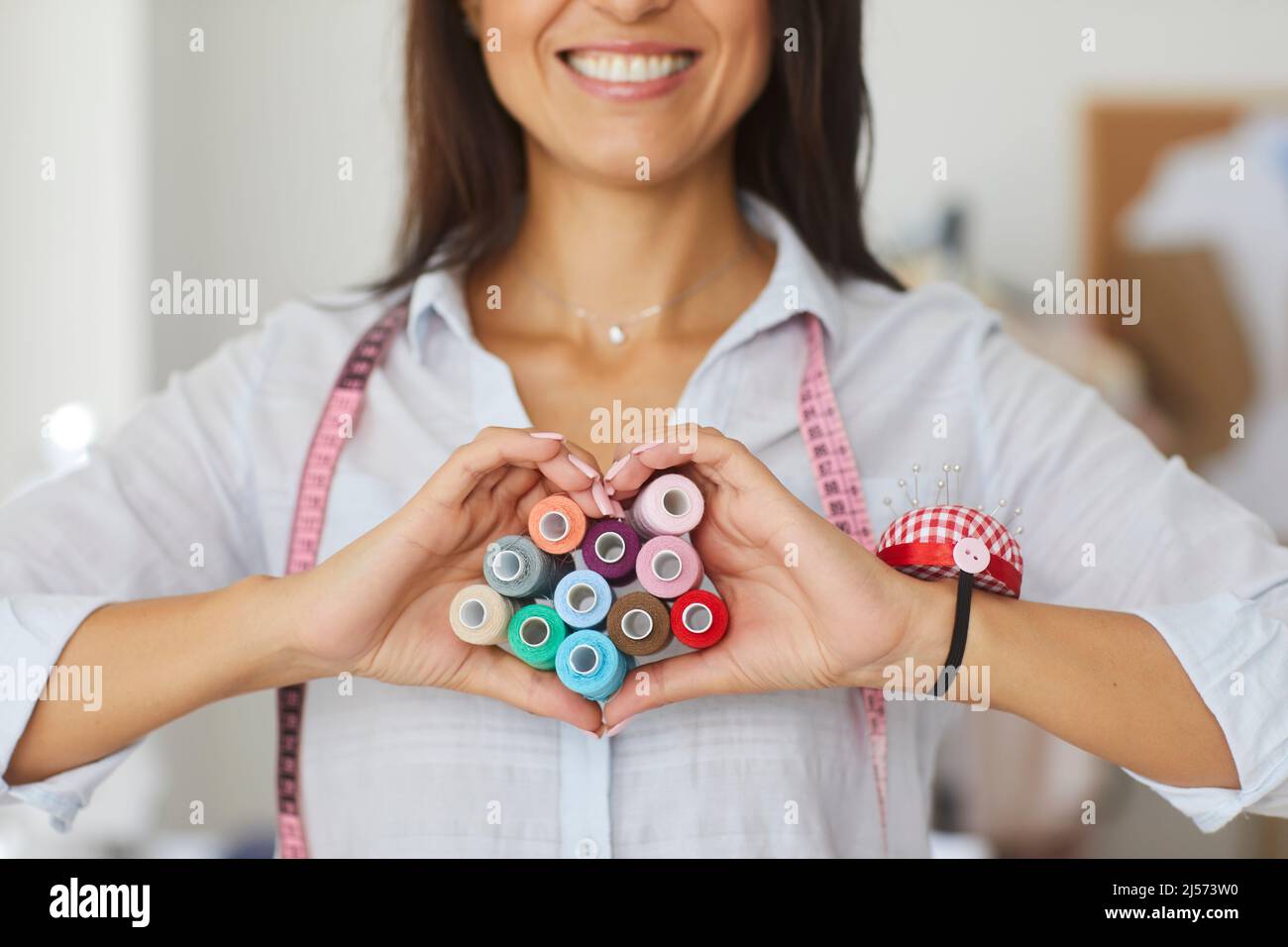 Lächelnde Schneiderin zeigt Herz Liebe Hand Geste Stockfoto