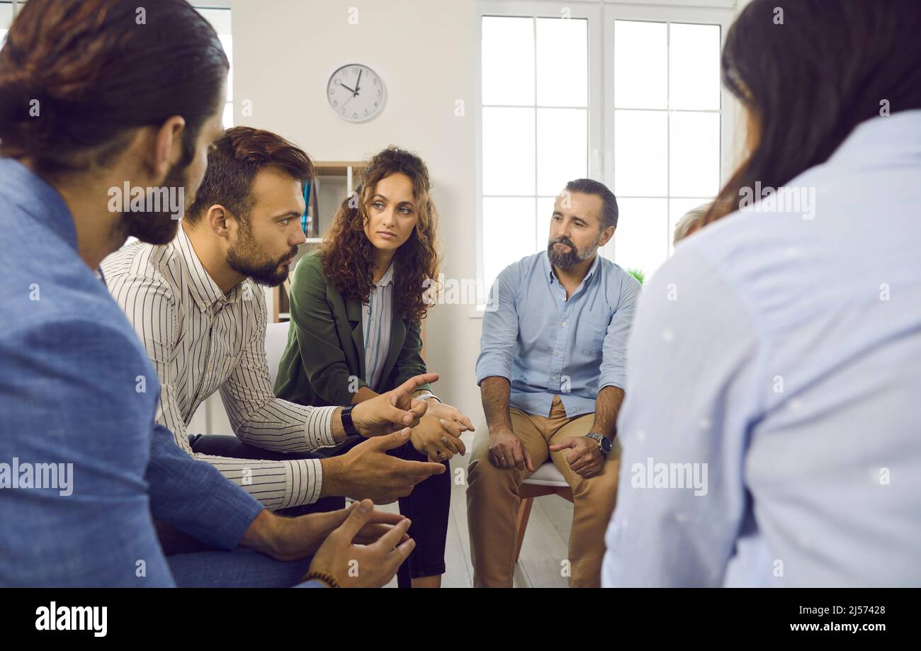 Personen, die im Kreis sitzen und dem Therapeuten während der Gruppentherapie zuhören Stockfoto