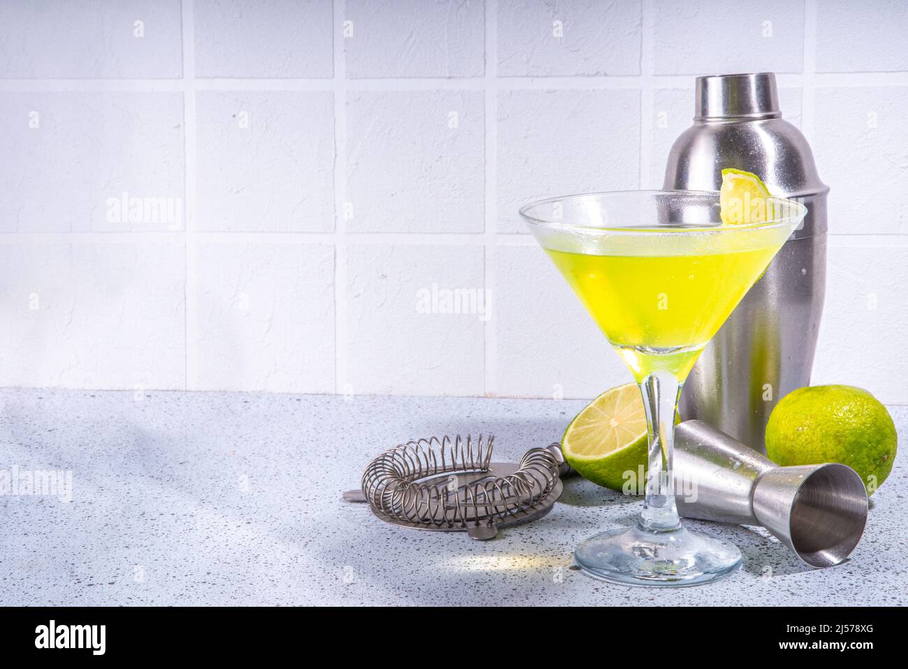 Klassischer Martini-Cocktail aus Lime Daiquiri mit Garnierung. Grüner Likör, Alkoholgetränk mit Barutensilien, heller Party-Cocktail im Sommer, weiß gefliester Backgrou Stockfoto