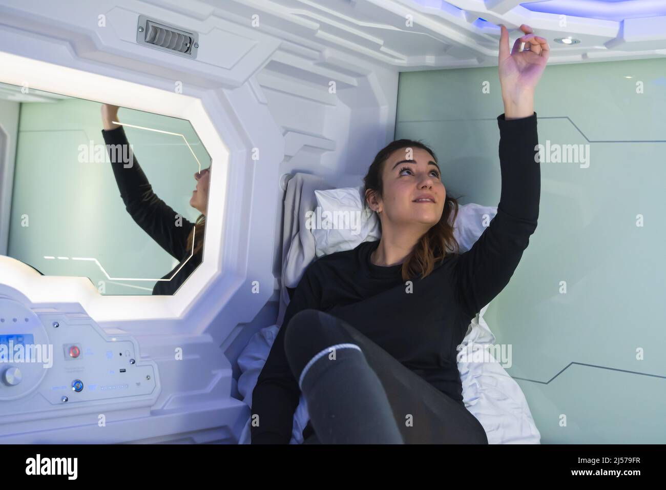 Hübsche Brünette Frau testet die Knöpfe in ihrer Kapsel Schlafzimmer Stockfoto