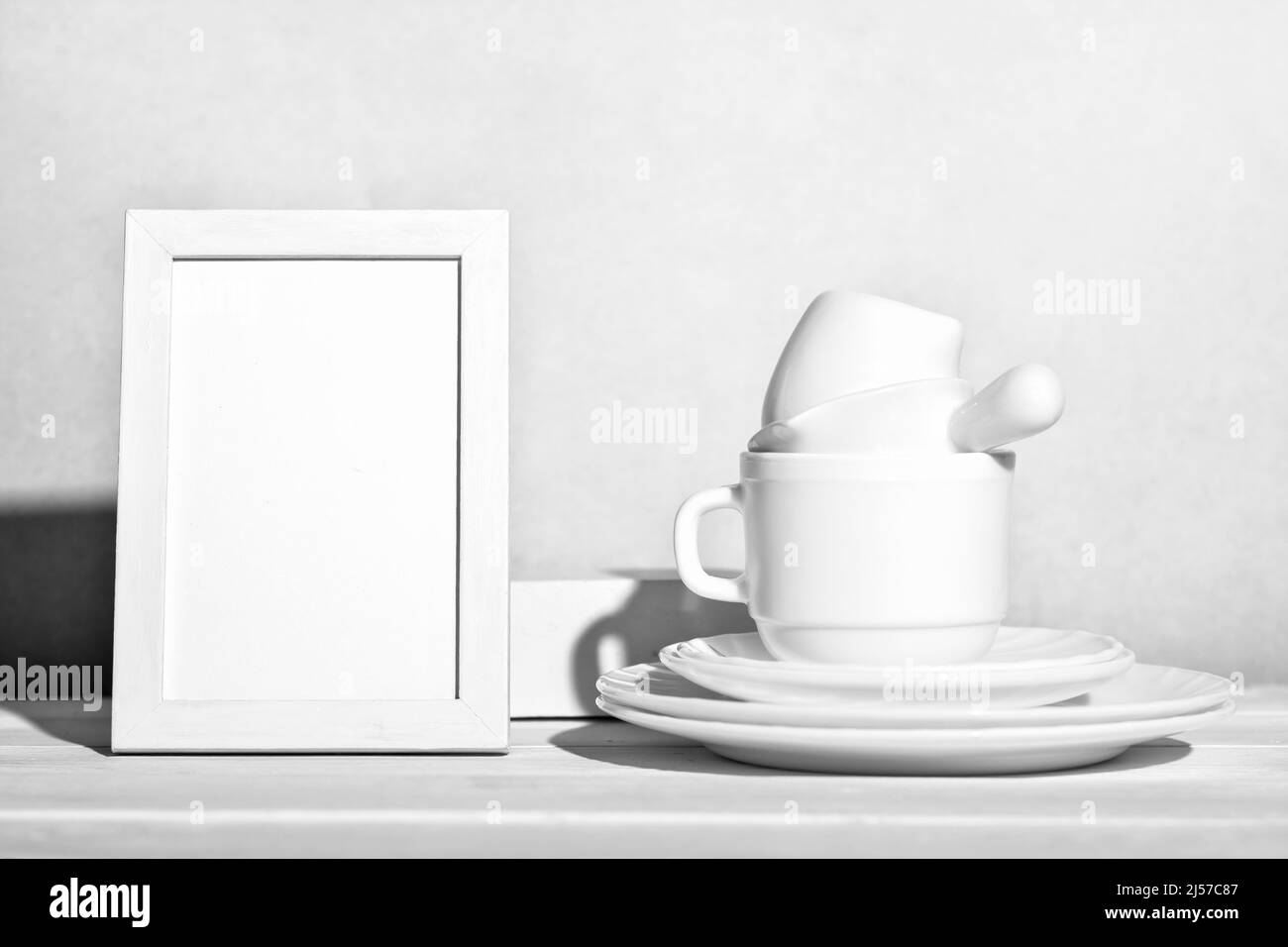 Weißes Geschirr und leerer Rahmen auf Holztisch. Geschirr und Teetasse neben weißem Rahmen mockup gestapelt. Copy Raum. Traditionelle Geschirr, Küche Reinigungskonzept Stockfoto