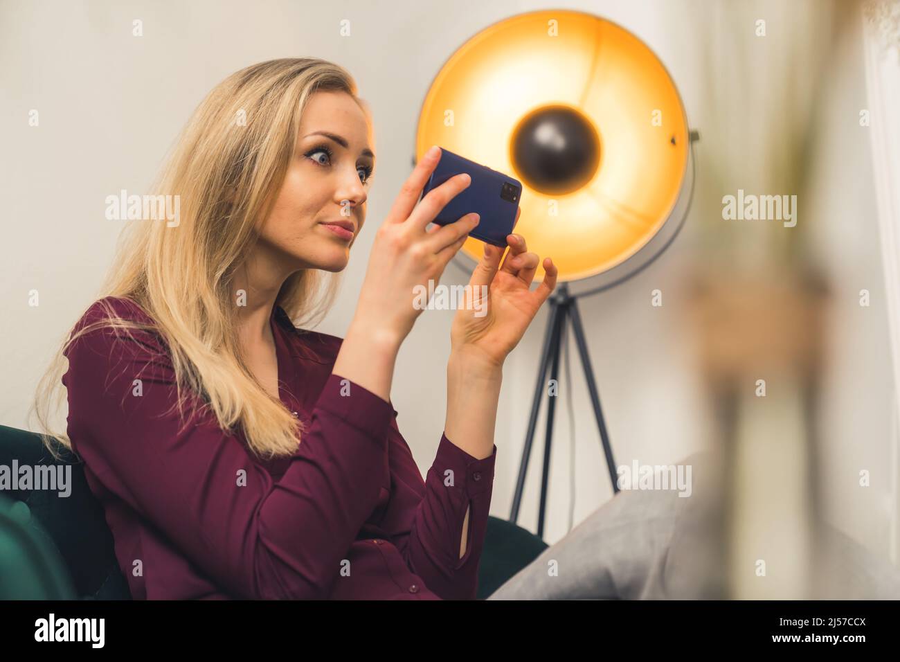 Junge kaukasische blonde Frau schaut auf ihr Smartphone im Wohnzimmer sitzen Kopie Raum . Hochwertige Fotos Stockfoto