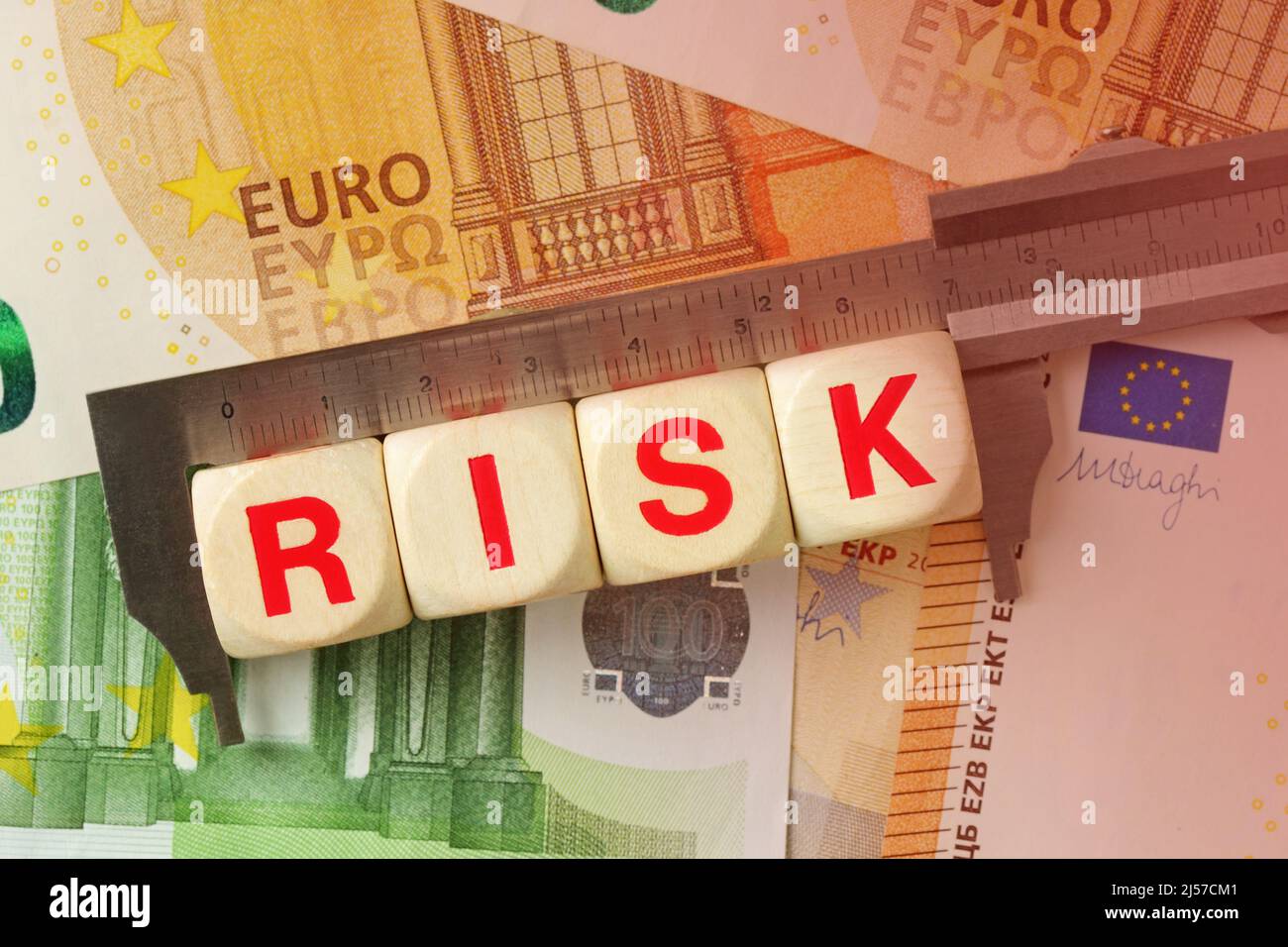 Messschieber und Holzklötze mit dem Wort Risiko auf dem Euro-Geld-Hintergrund - Konzept des Euro und des finanziellen Risikos Stockfoto