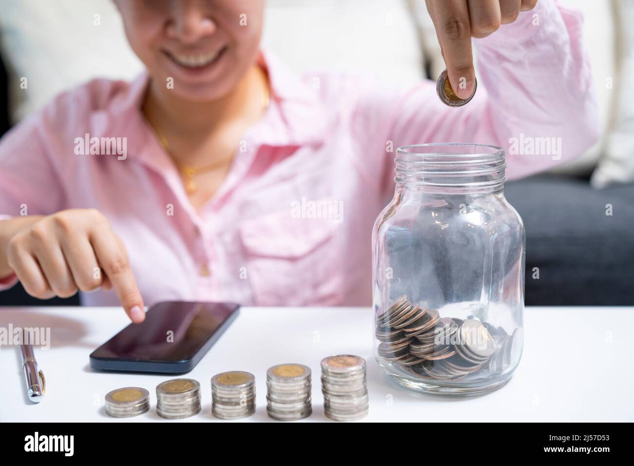 Weiblich rechnen über Geld sparen und legen Münze in Glas auf den Schreibtisch zu Hause. Stockfoto