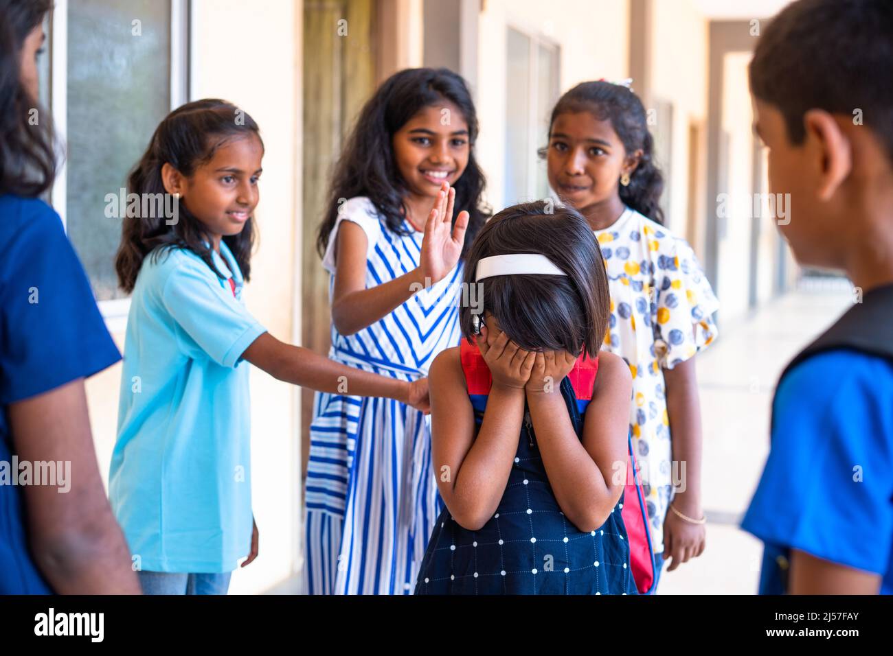 Gruppe von Kindern, die Mädchen auf dem Schulkorridor umzingeln - gekonntes Gezeter, Drohgebärden und soziale Ablehnung Stockfoto