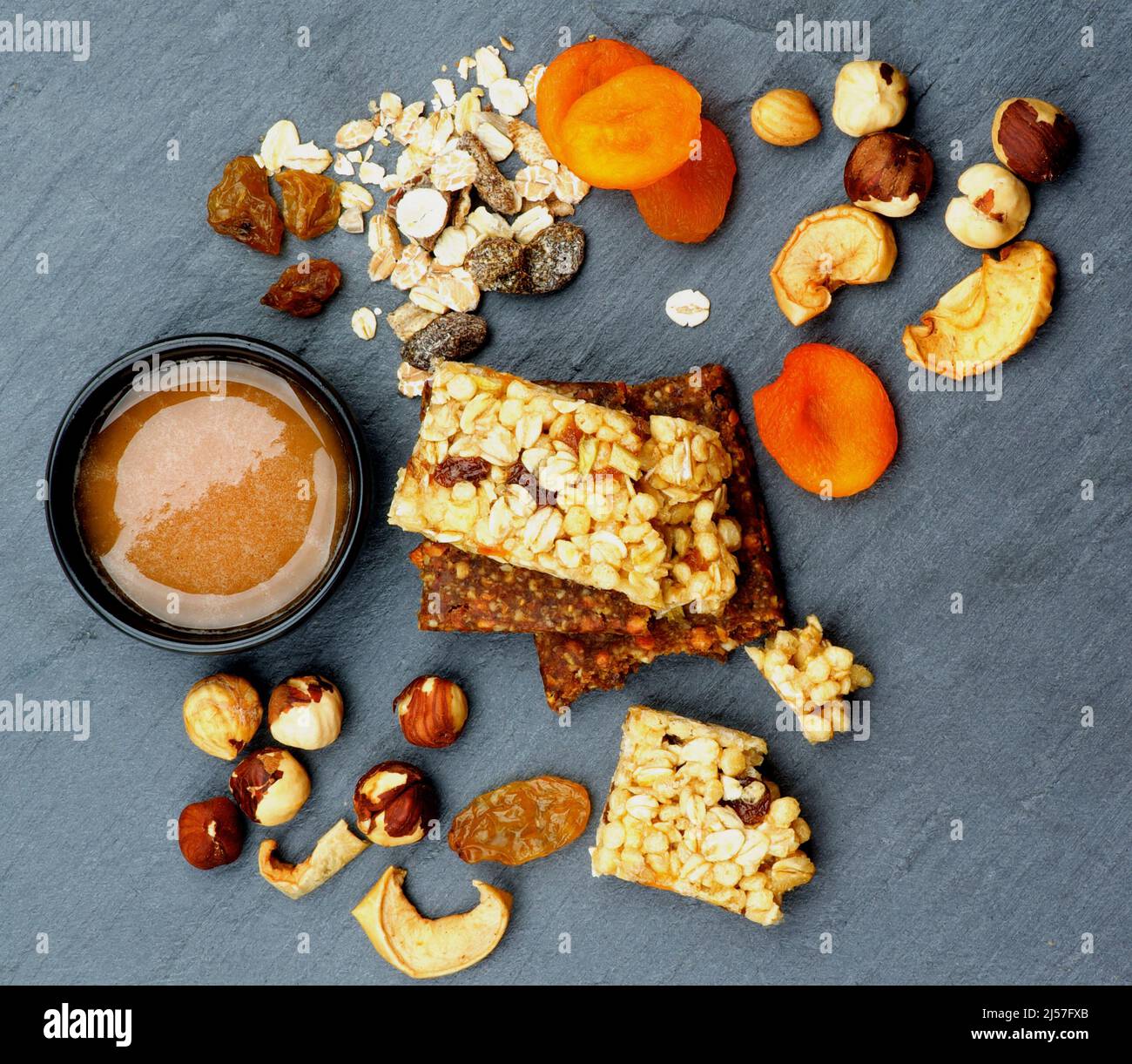 Arrangement von nützlichen Müsliriegel mit Müsli, Nüssen, getrockneten Aprikosen und einer Schüssel Honig auf schwarzem Stein Hintergrund. Draufsicht Stockfoto