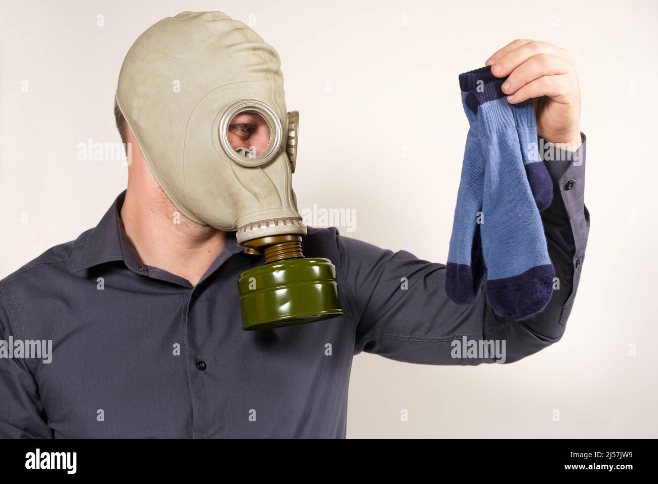 Ein Mann in einer Gasmaske hält schmutzig riechende Socken. Das Problem des unangenehmen Fußgeruchs bei Männern Stockfoto