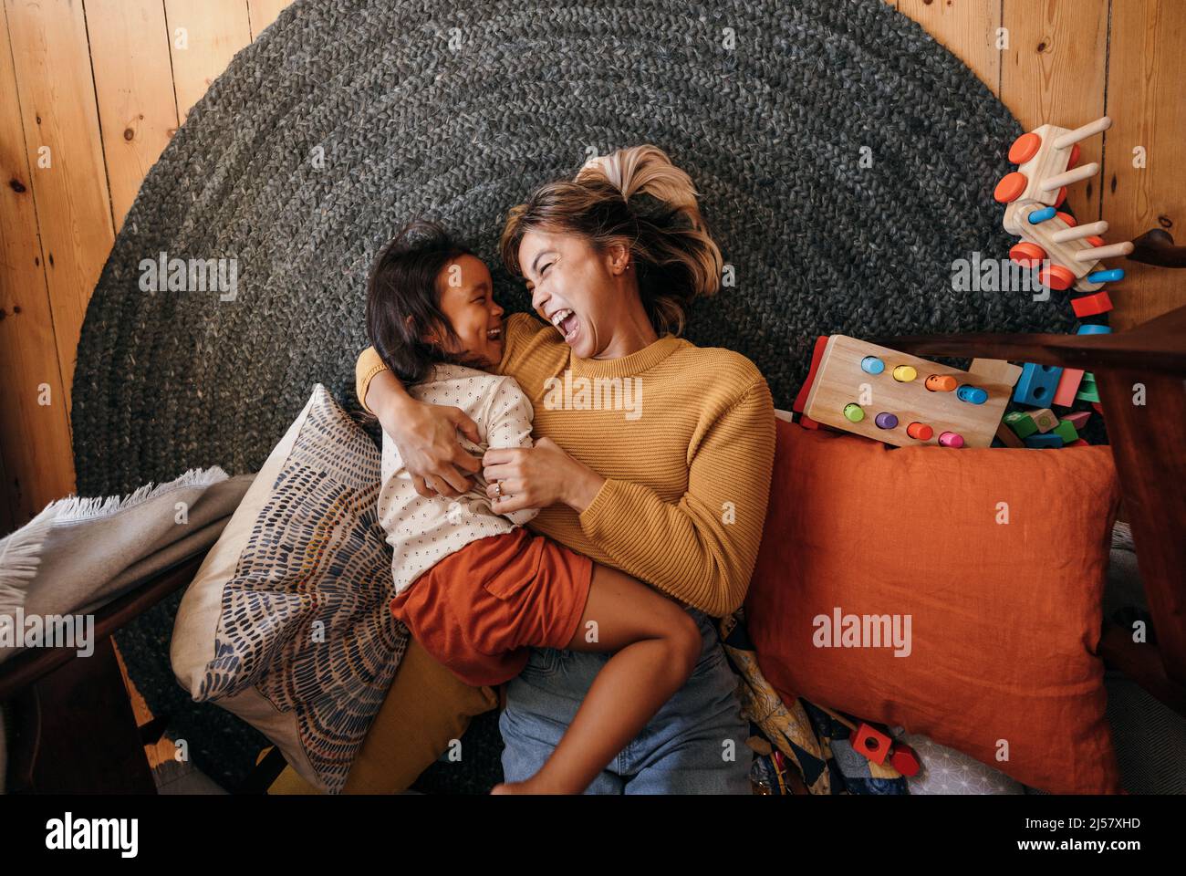 Draufsicht auf eine Mutter und ihre Tochter, die zu Hause fröhlich lachen. Glückliche Mutter und Tochter liegen auf dem Boden in ihrem Spielplatz. Mutter und Tochter Stockfoto
