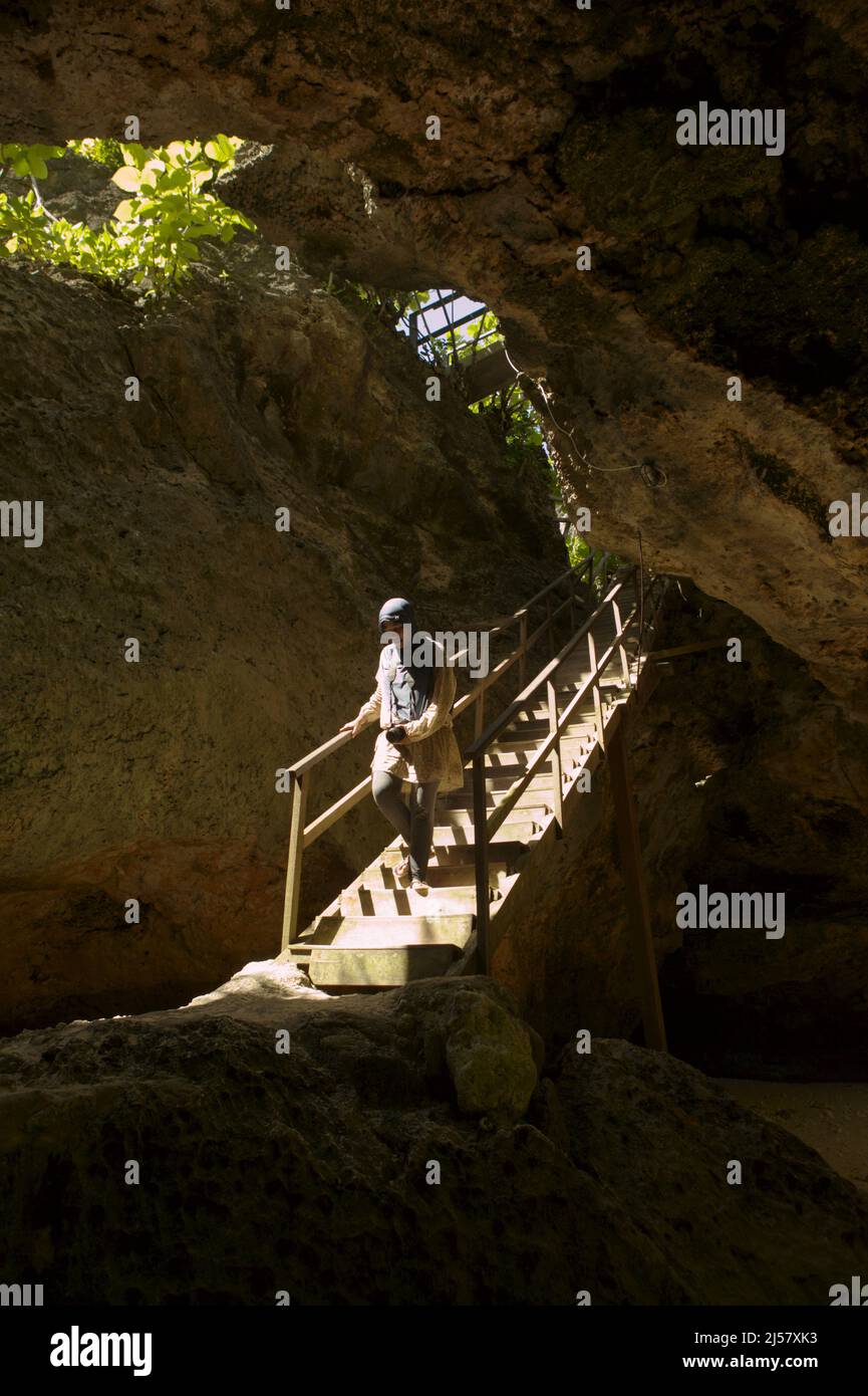 Eine Frau, die eine Treppe durch eine Kalksteinhöhle hinuntergeht, die zum Strand Padang-padang in Labuan Sait, Süd-Kuta, Bali, Indonesien führt. Stockfoto