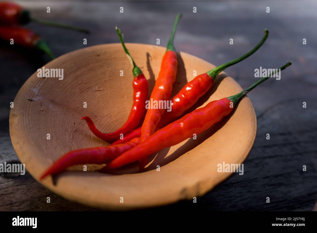 Eine Nahaufnahme von roten langen Chilischoten mit grünen Kappen auf einer Holzoberfläche. Stockfoto