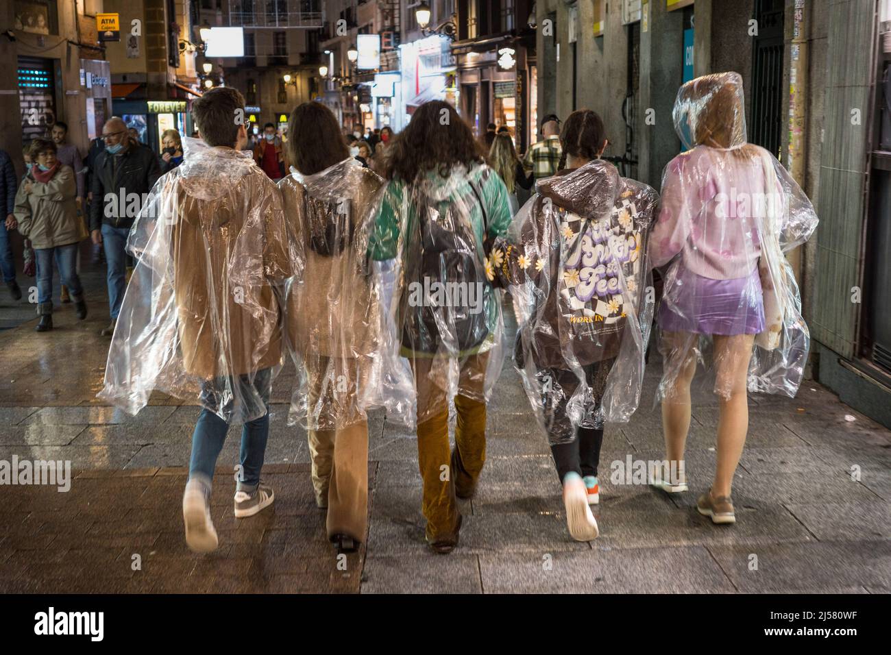 Eine Gruppe junger Menschen, die im Regen in transparenten Einweg-Regenmänteln aus Kunststoff spazieren, Madrid, Spanien. Stockfoto