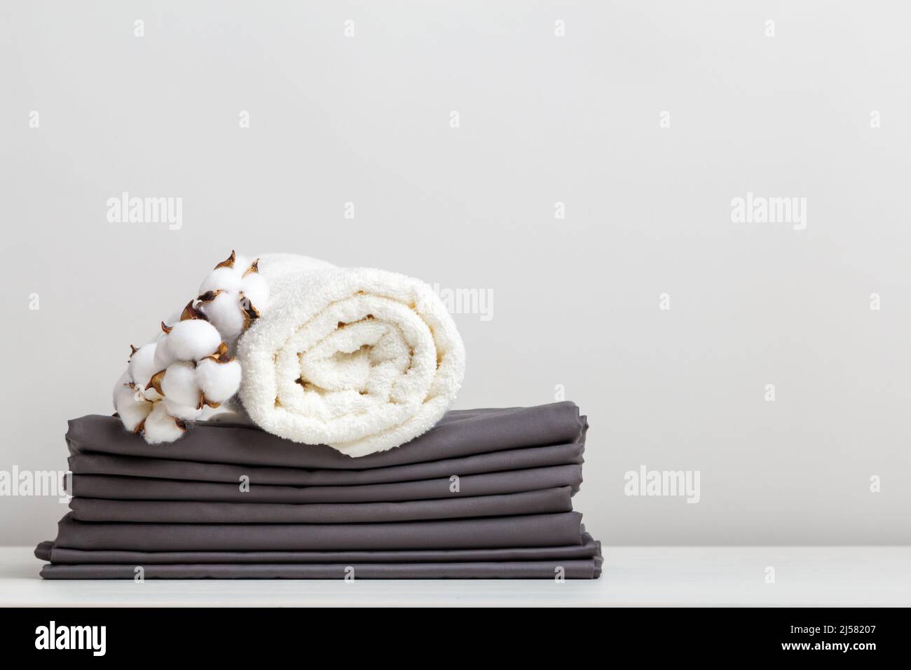 Ein Stapel grauer Bettwäsche, Laken und ein Frottee weißes Handtuch auf dem Tisch. Stockfoto