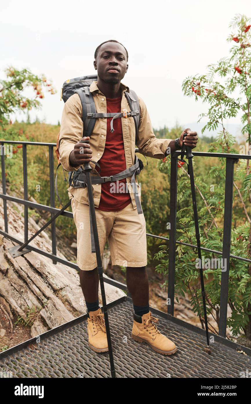 Porträt eines hübschen jungen Afro-Amerikaners mit Rucksack, der mit Spazierstöcken auf einer Brücke im Freien steht Stockfoto