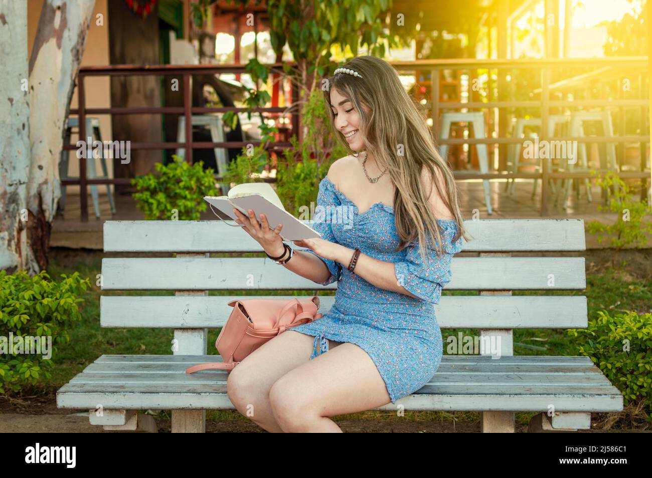 Ein süßes Mädchen, das auf einer Bank sitzt und ein Buch liest, ein hübsches junges lateinisches Mädchen, das ein Buch auf einer Bank liest Stockfoto