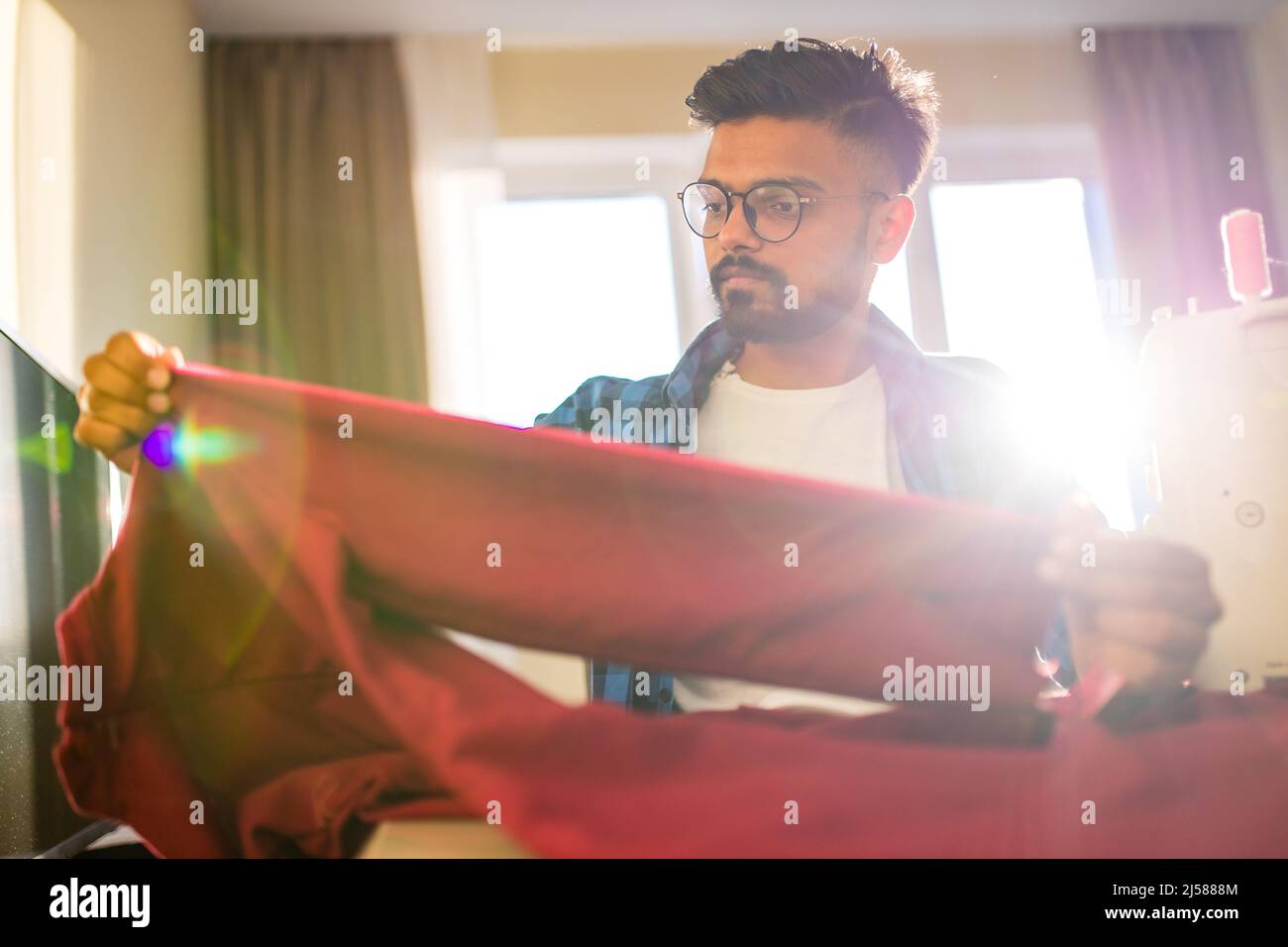 indische Schneider asiatische Mann Designer nähen Kleidung auf Nähmaschine neben Laptop Wohnung Arbeitsplatz Stockfoto