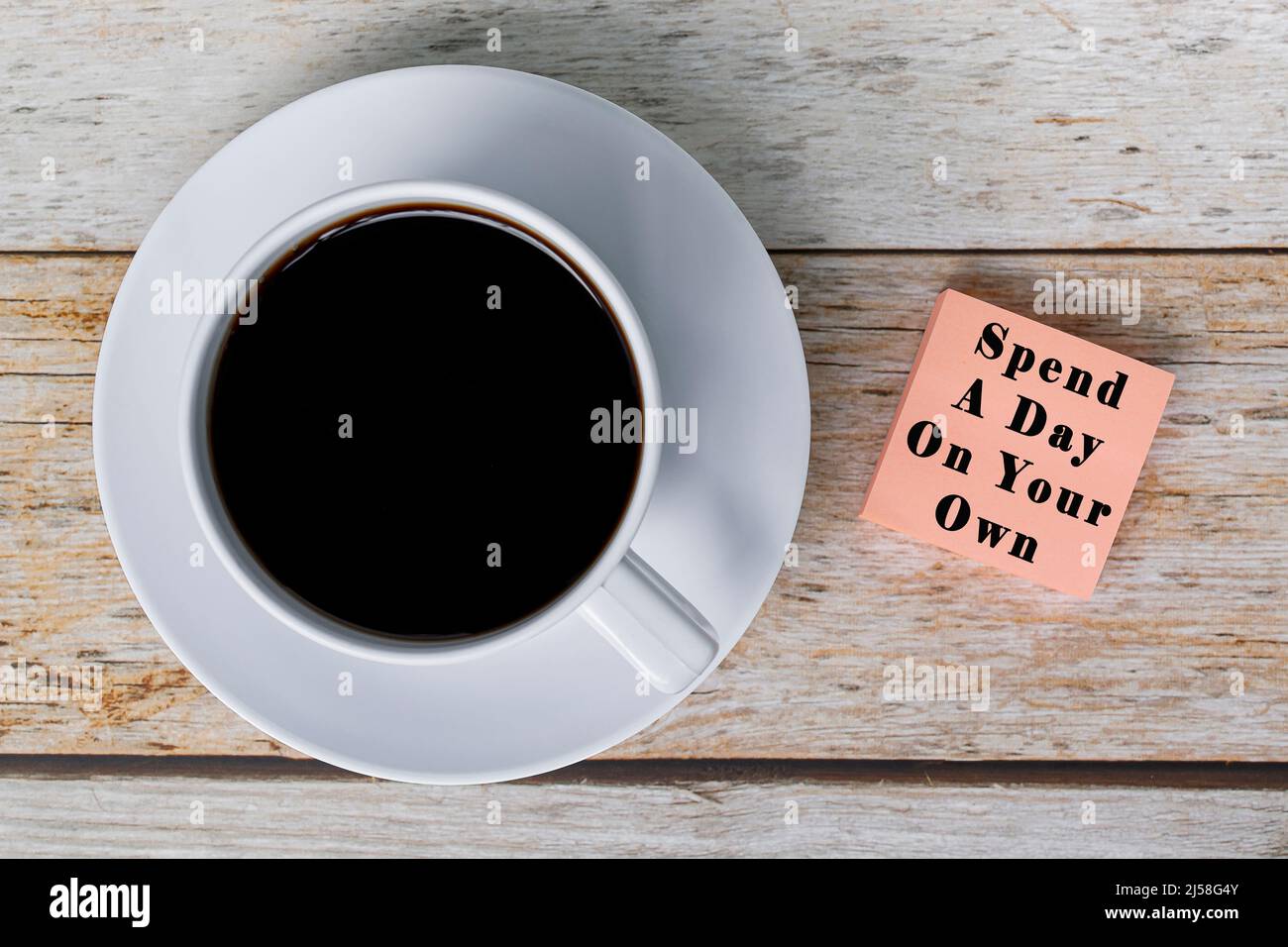 Motivierendes Zitat auf Notizblock mit weißer Kaffeetasse auf Holzschreibtisch - verbringen Sie einen Tag auf eigene Faust. Stockfoto