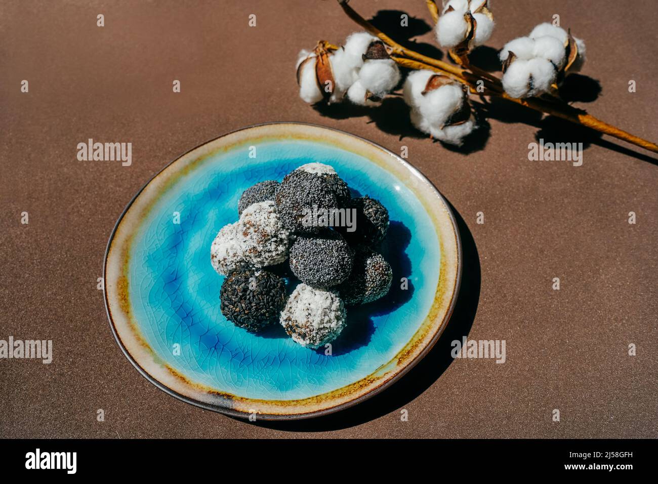 Hausgemachte Bonbons mit Mohn, Sesam und Kokosraspeln. Blaue Platte auf braunem Hintergrund. Stockfoto