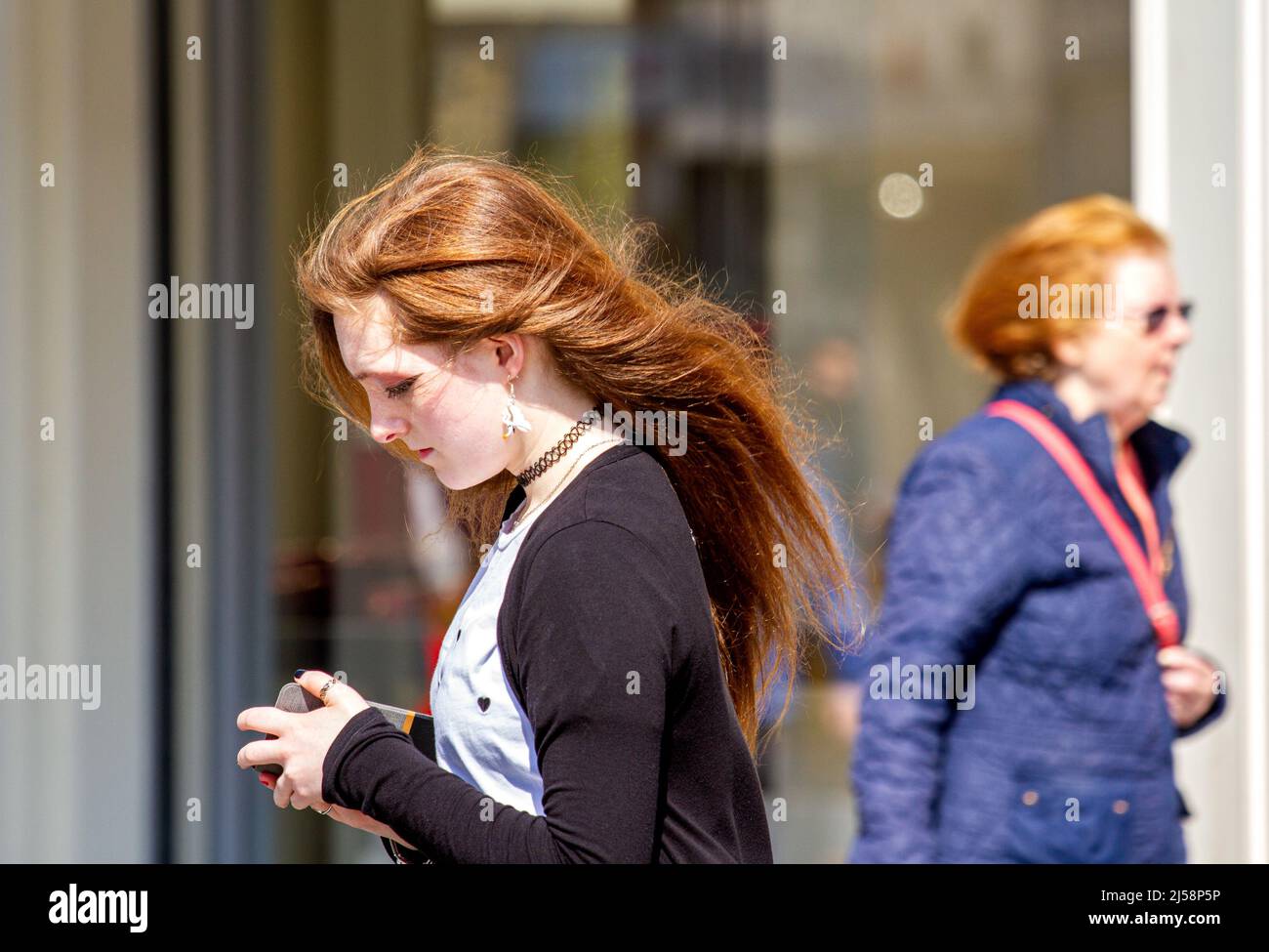 Dundee, Tayside, Schottland, Großbritannien. 21. April 2022. UK Wetter: Aufgrund der kühlen stürmischen Winde und der warmen Frühlingssonne erreichten die Temperaturen in Nordostschottland 15 Grad Die Anwohner sind im Stadtzentrum von Dundee unterwegs, um sich in der milden und windigen Aprilsonne mit Freunden zu unterhalten, aber die Haare einer Frau wehen im Wind, was sie zu einem schlechten Haartag führt. Kredit: Dundee Photographics/Alamy Live Nachrichten Stockfoto