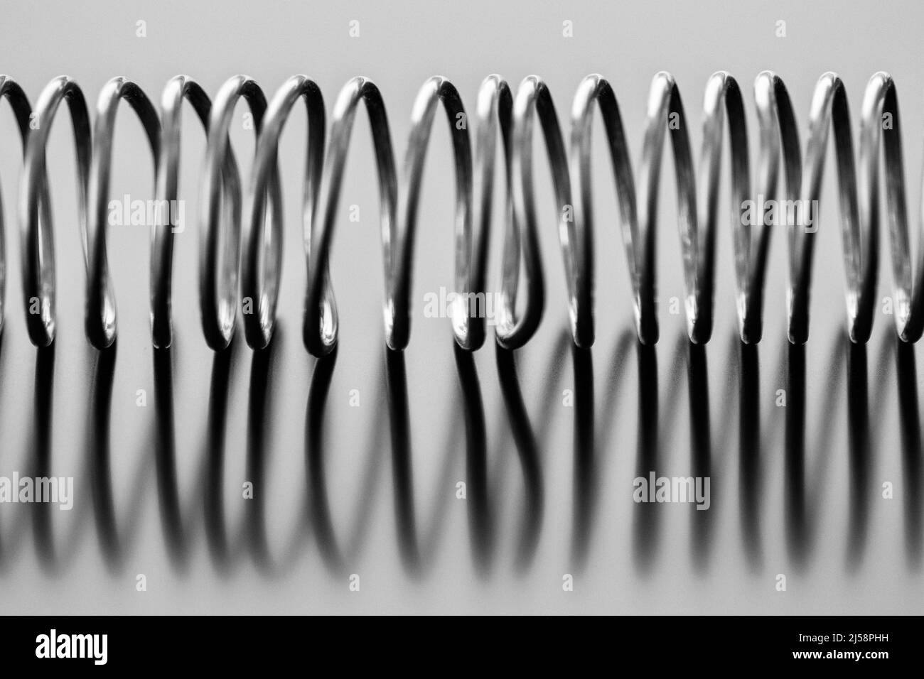 Eine Spirale aus Bleidraht, geformt in eine Spirale, auf einer reflektierenden Oberfläche, ergibt ein abstraktes Design. Stockfoto