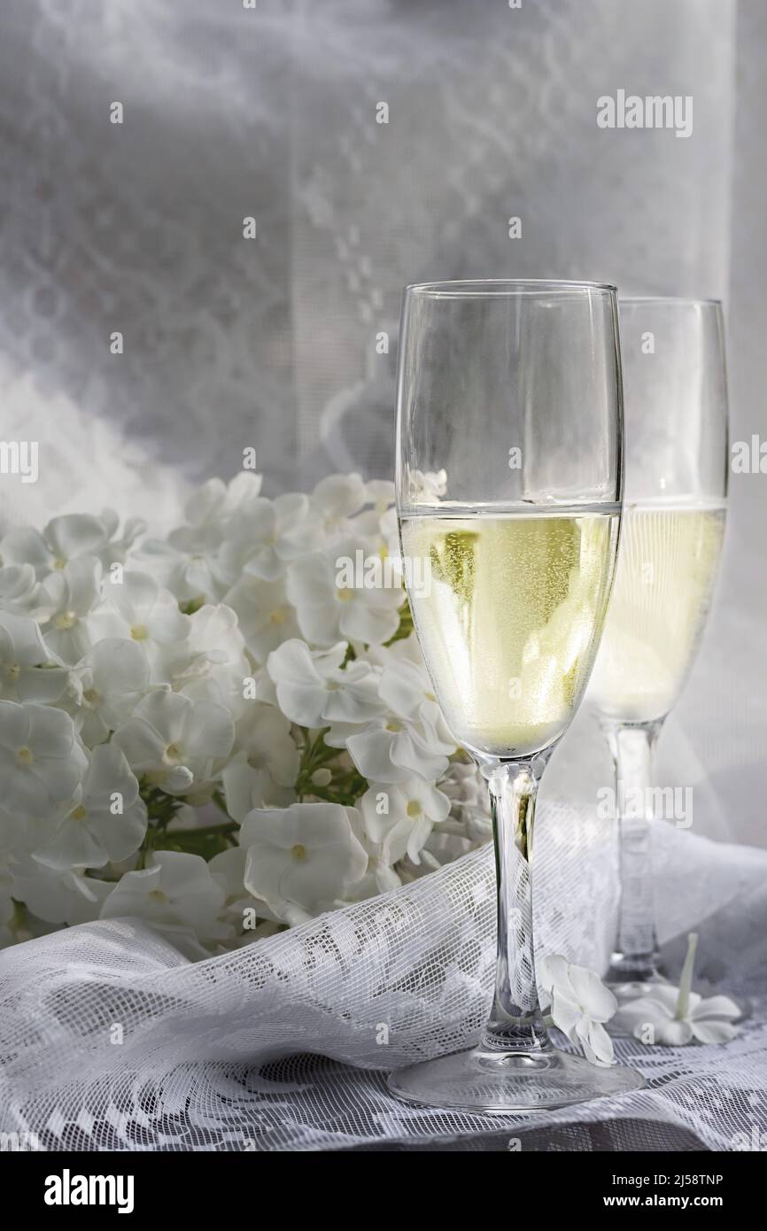 Zwei Gläser Champagner auf einem Hintergrund aus weißen Phlox-Blumen für eine romantische Feier mit Platz zum Kopieren Stockfoto