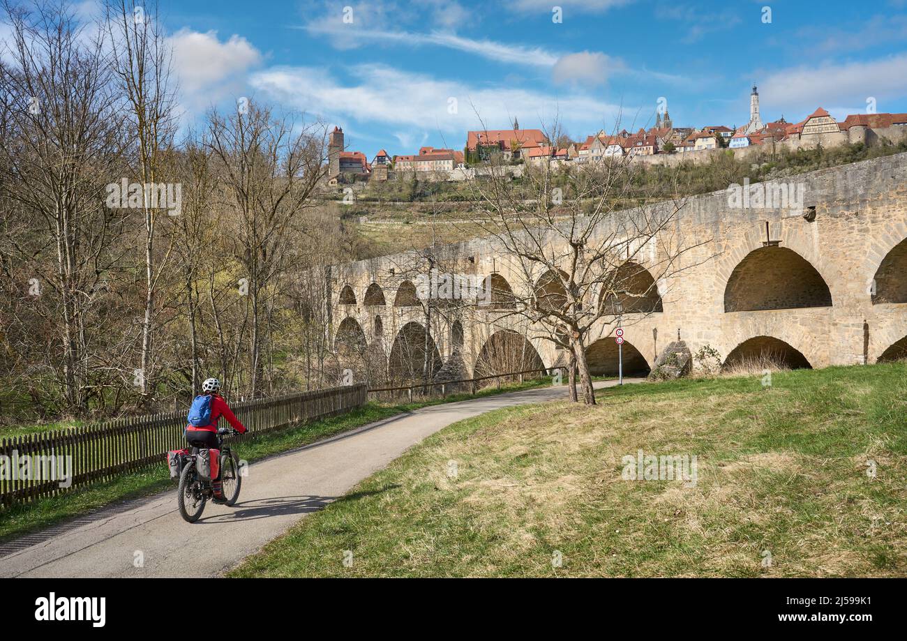 Nette Stadtfrau auf einer Radtour auf der berühmten deutschen Schlossroute, unterhalb der mittelalterlichen Skyline von Rothenburg ob der Tauber, Bayern, Deutschland Stockfoto