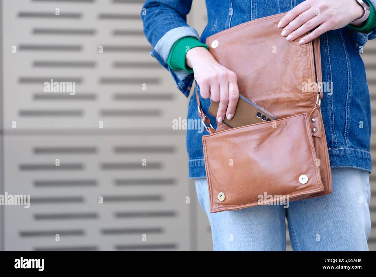 Frau, die das Mobiltelefon in eine braune Lederhandtasche in Nahaufnahme legt Stockfoto