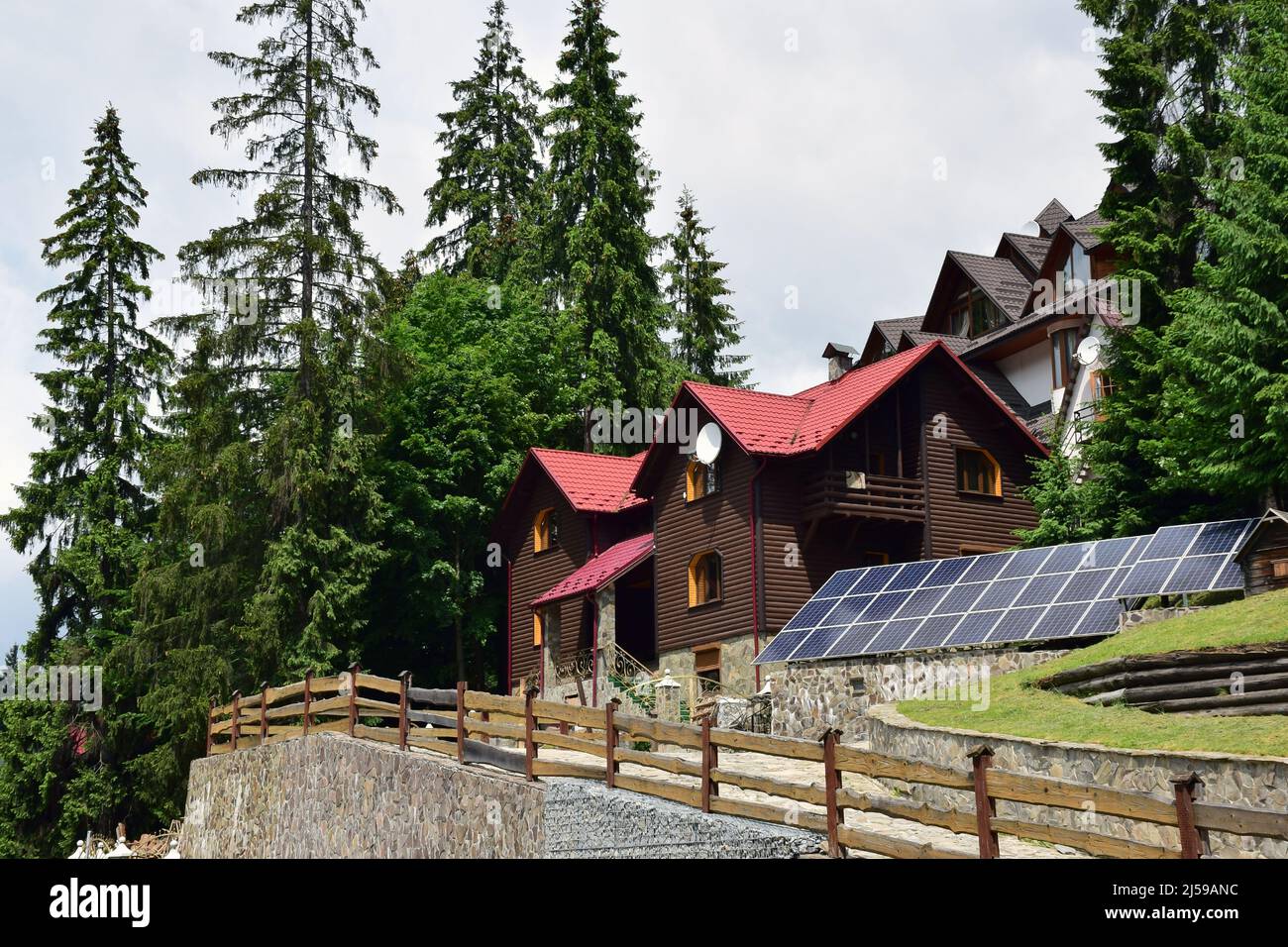 Hütten in einem Bergwald, in der Nähe der Reihen von ökologischen Solarzellen für erneuerbare Elektrizität Stockfoto