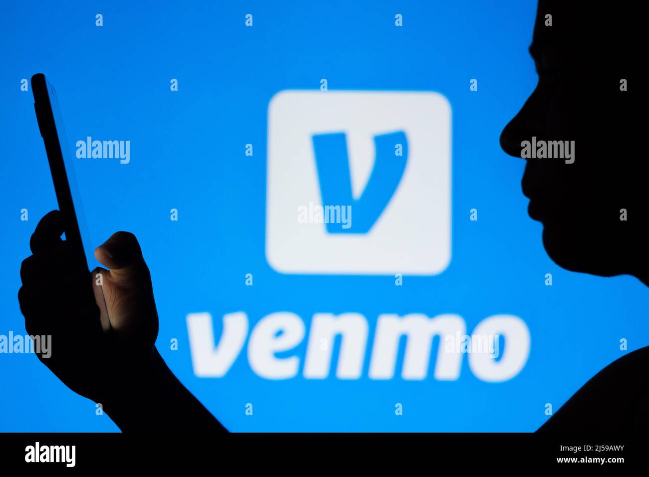 Auf dieser Fototafel ist das Venmo-Logo zu sehen, das im Hintergrund einer Frau mit Silhouetten in der Hand eines Mobiltelefons zu sehen ist. Stockfoto