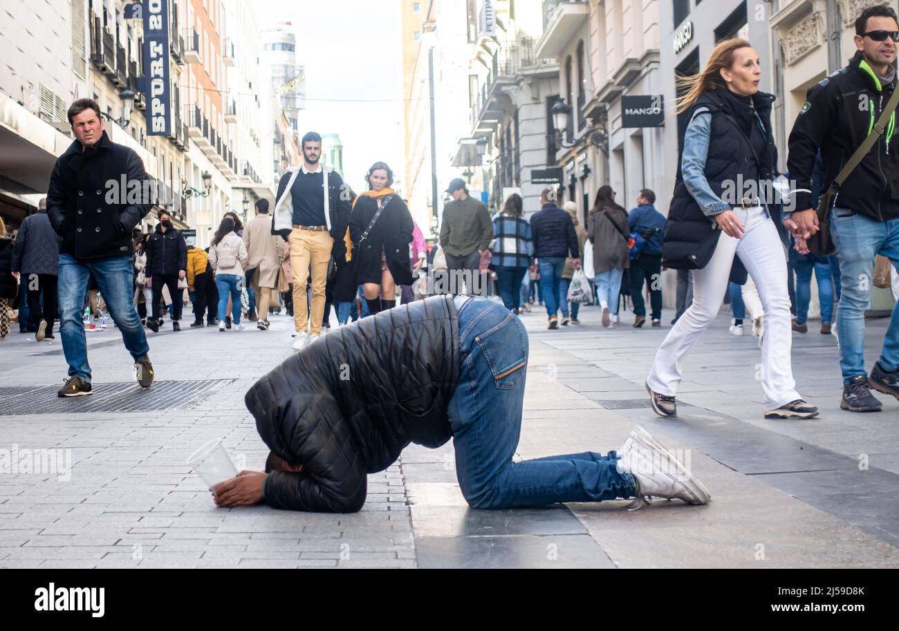 Ein Mann auf den Knien und mit dem Kopf auf den Boden, mit einem Plastikbecher, der um Geld bettelte, im Zentrum von Madrid, Spanien Stockfoto
