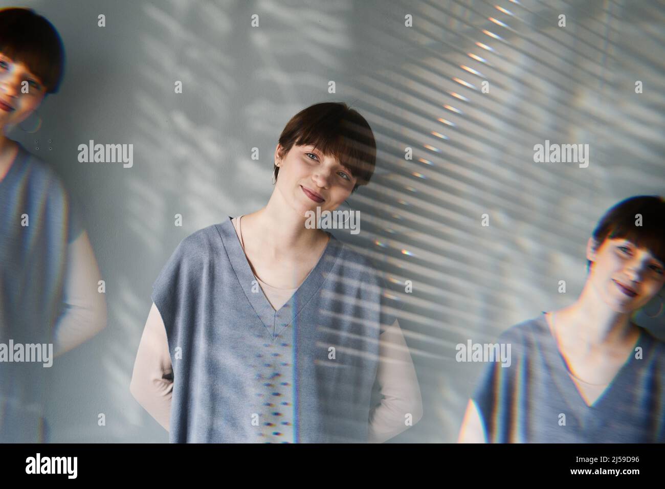 Mehrere Aufnahmen einer lächelnden hübschen Frau mit kurzen Haaren, die mit den Händen hinter der Wand steht Stockfoto