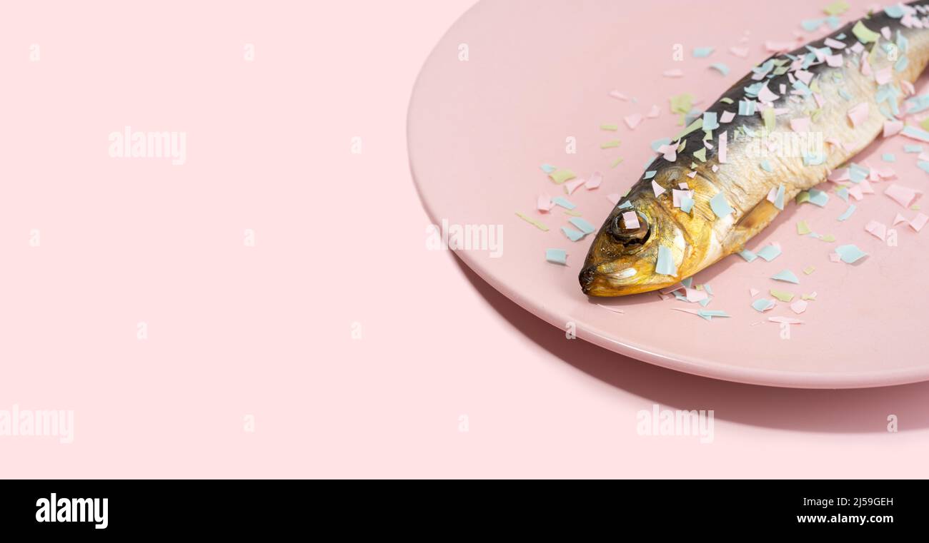 Fisch bedeckt Mikroplastik auf einem rosa Teller. Auswirkungen von Mikroplastik auf die Lebensmittelkette. Die Idee der Mikroplastik Verschmutzung. Konzept der Umgebung Stockfoto