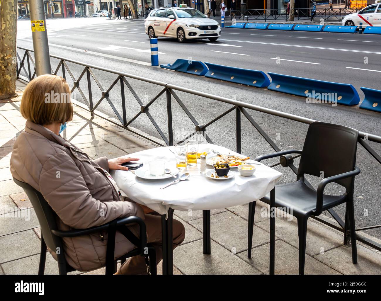 Eine Frau allein, die im Winter in Madrid, Spanien, Kaffee und Dessert im Café im Freien am Tisch in der Nähe der Straße getrunken hat Stockfoto