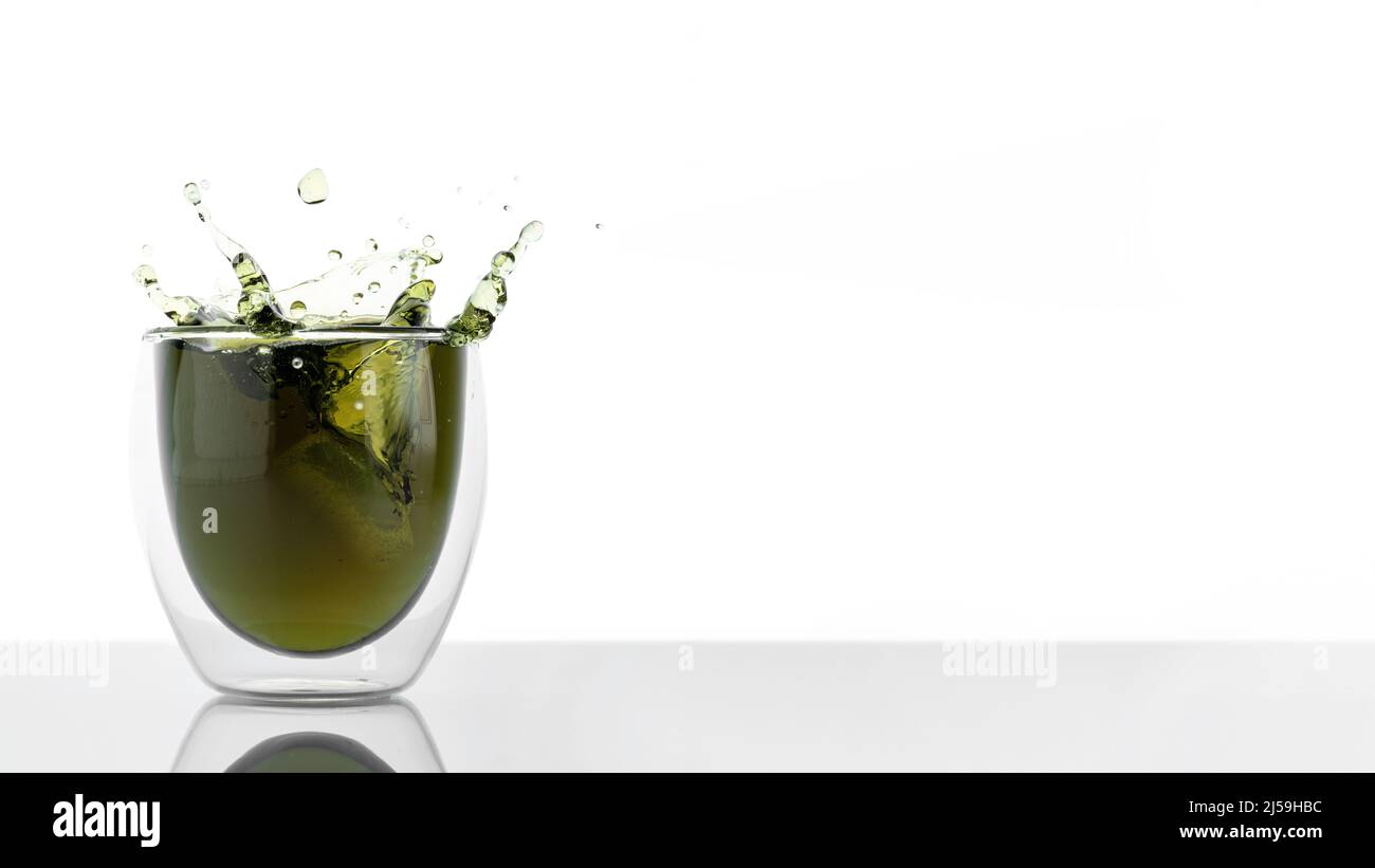 Glas Wasser mit Chlorophyll-Extrakt vor weißgrauem Hintergrund. Flüssiges Chlorophyll in einem Glas Wasser mit Spritzern. Konzept von Superfood Stockfoto
