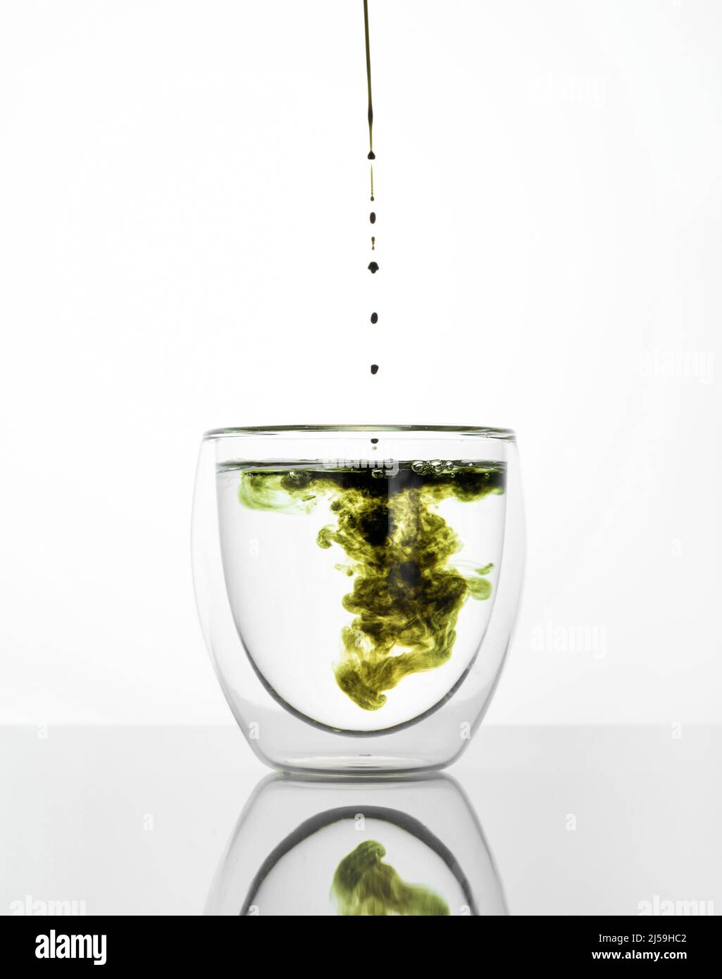 Glas Wasser mit Chlorophyll-Extrakt vor weißgrauem Hintergrund. Flüssiges Chlorophyll in ein Glas Wasser gießen. Konzept von Superfood, Gesundheit Stockfoto