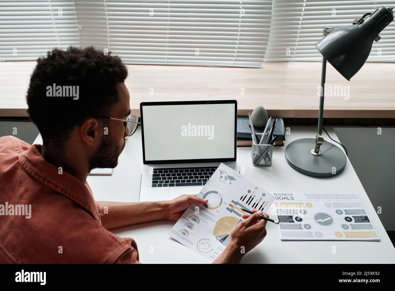 Beschäftigt schwarzer strategischer Manager mit Brille, der am Schreibtisch sitzt und im Büro mit analytischen Daten arbeitet Stockfoto