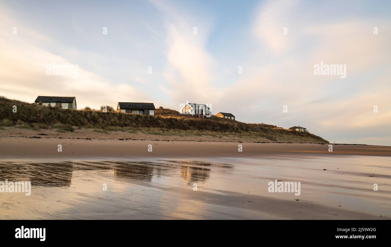 Weiches Abendlicht hebt verstreute Strandhütten in den Dünen mit Blick auf die Embleton Bay an der Küste von Northumberland hervor. Stockfoto