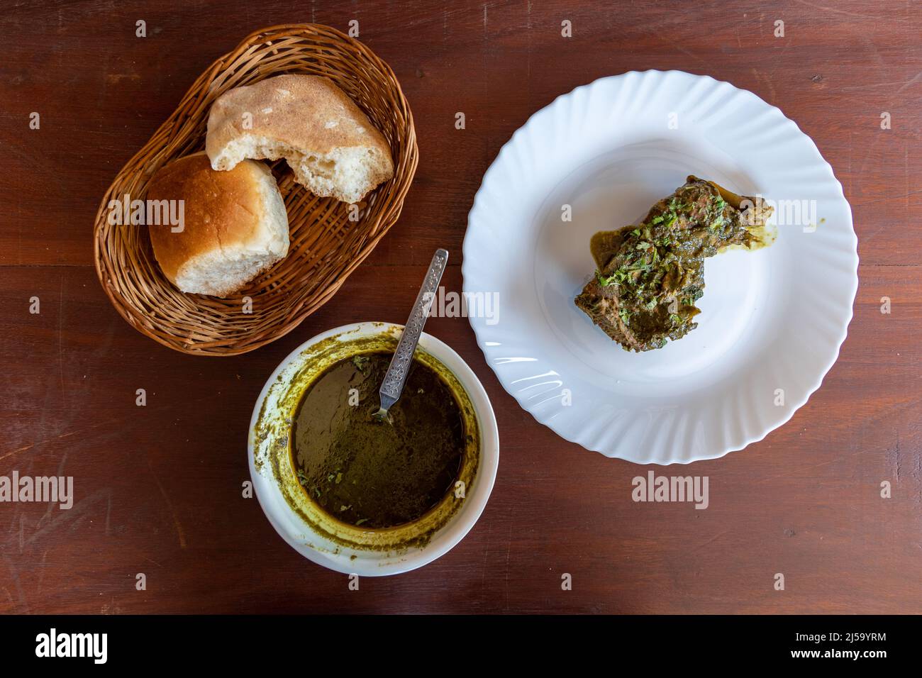 Draufsicht auf authentisches Goan-Gericht, Hühnchen-Cafreal und halbgessenes Goan-Brot Stockfoto