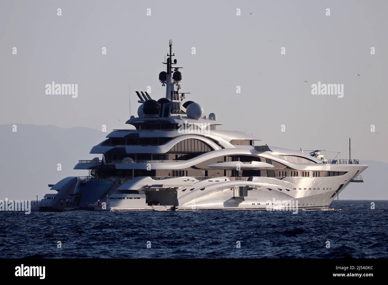 Luxusyacht mit Hubschrauberlandeplatz segelt im Meer, Seitenansicht. Futuristisches Boot auf nebligen Bergen Hintergrund am Morgen Stockfoto