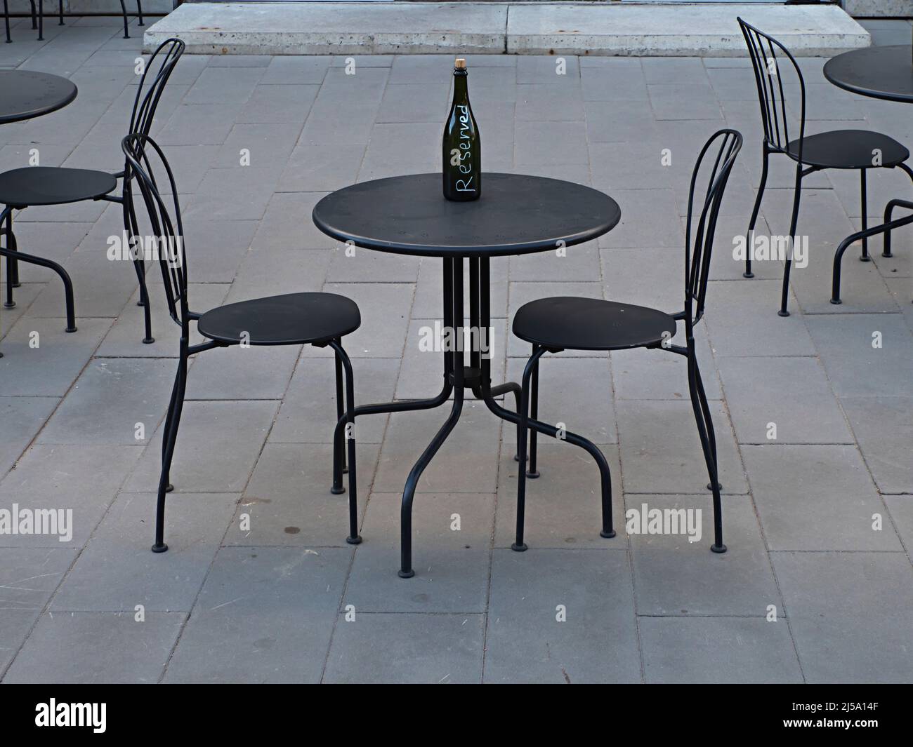 Metallloft mit schwarzen Metalltischen und -Stühlen und einer leeren Flasche mit Sekt, die als reserviert auf einer Terrasse im Freien im Industriestil gekennzeichnet ist Stockfoto