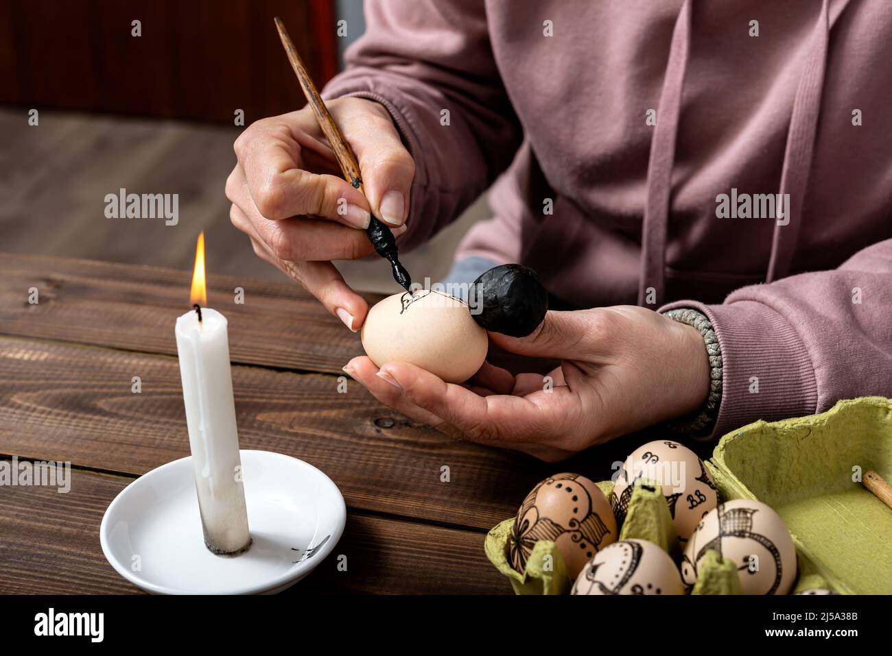 Weibliche Hände malen traditionell Eier mit Blumenmustern mit einem Füllfederhalter und Wachs für Ostern auf einem Holztisch. Ostervorbereitungskonzept. Stockfoto