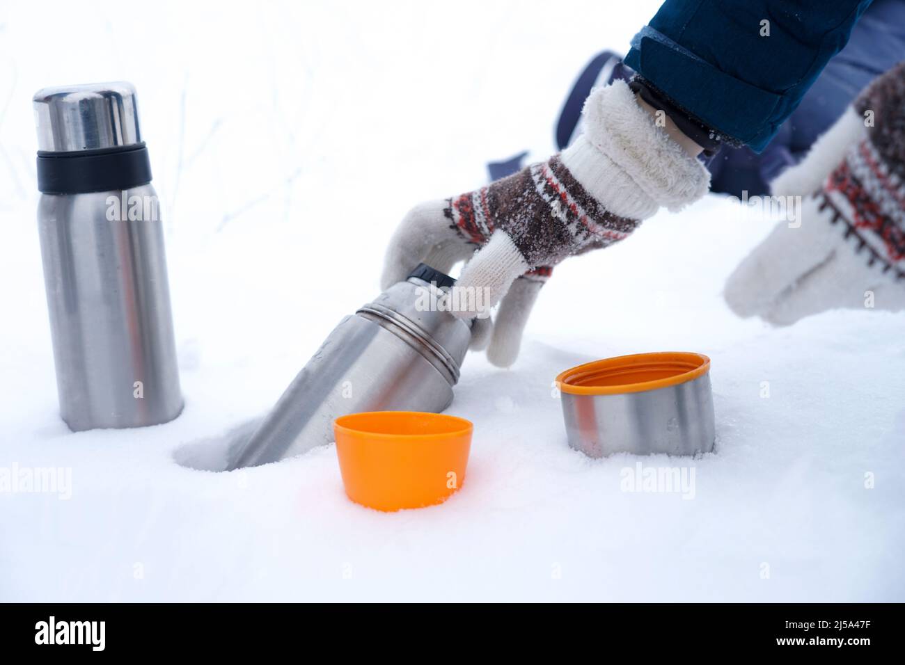 Hände in Handschuhen halten eine Thermoskanne auf dem Schnee. Tee in einer Thermoskanne im Winter auf dem Schnee Stockfoto