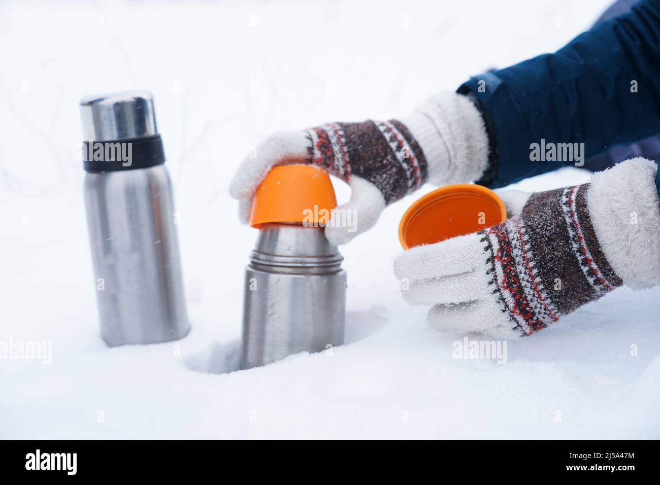 Hände in Handschuhen halten eine Thermoskanne auf dem Schnee. Tee in einer Thermoskanne im Winter auf dem Schnee Stockfoto