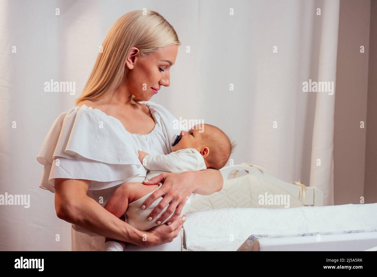 kaukasische Mutter, die Babypuder aufbringt, bevor sie ihrem vier Monate alten Baby Windeln im Bett zu Hause aufsetzt Stockfoto